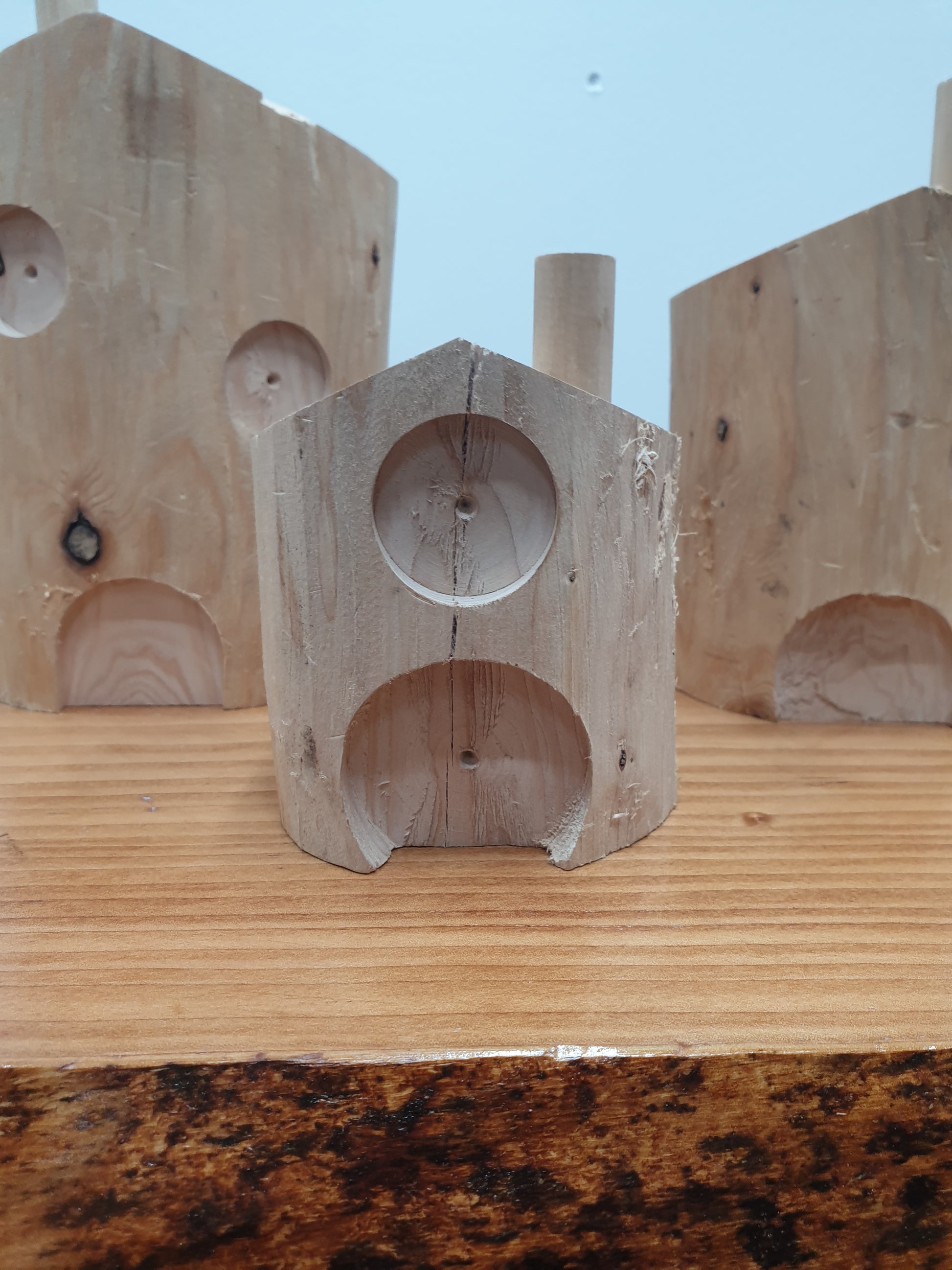 A close up of a 10cm untreated fairy house. It has a wide central door with a small round window directly above and a chimney on the right hand side of the roof.