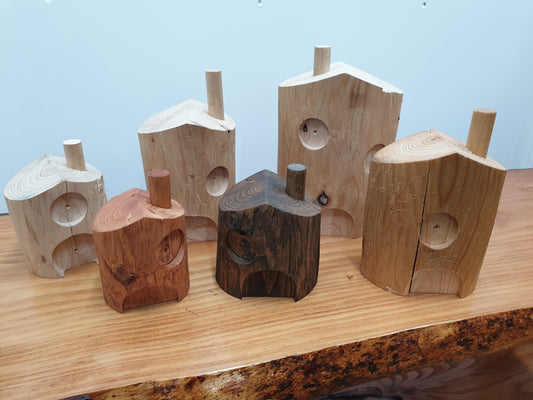 A photo of 6 fairy houses in all different shapes and sizes. Variations in door, window and chimney placement. There is one treated in red cedar oil, dark oak oil and normal danish oil, the other 3 are untreated.