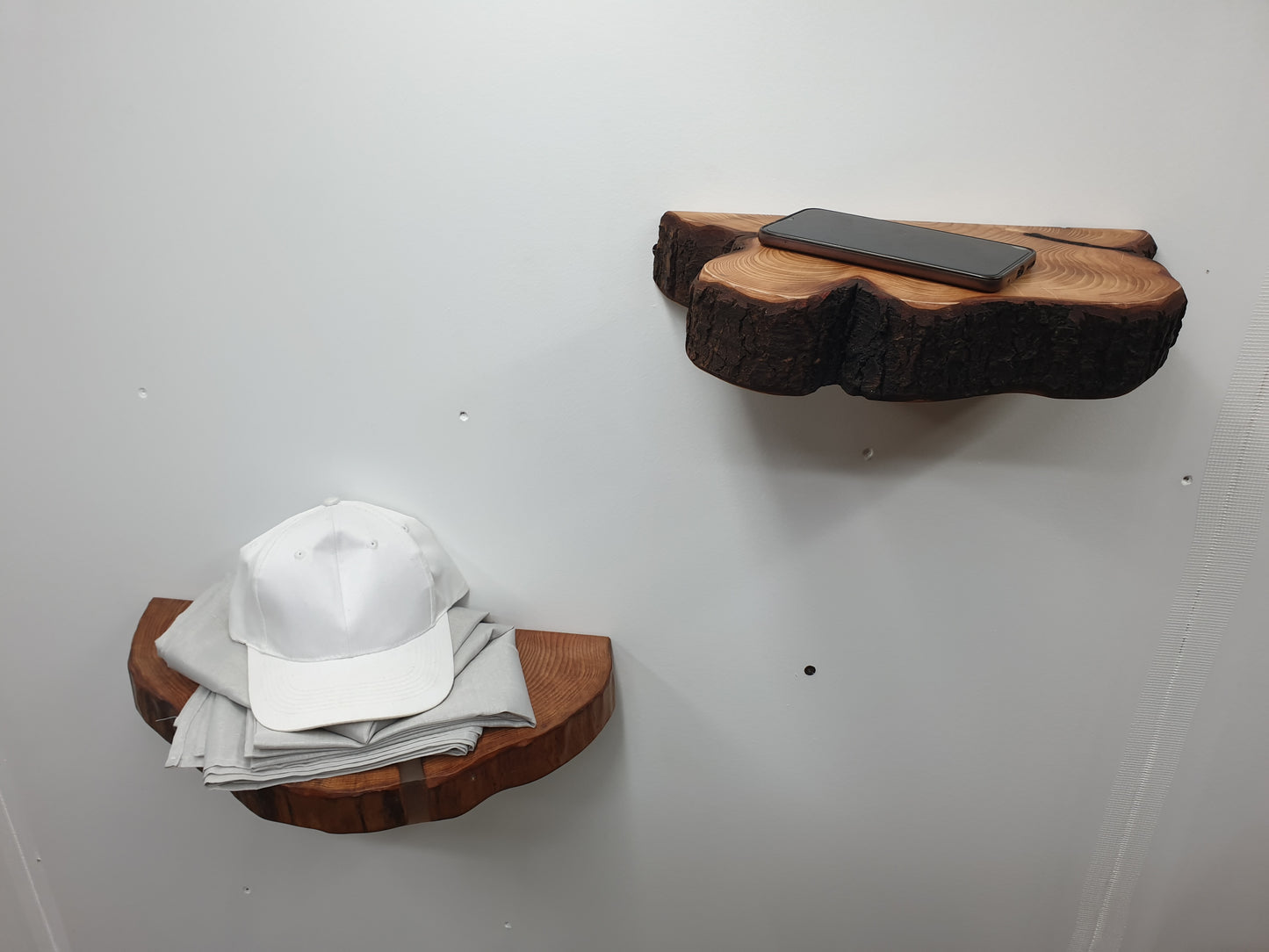 a pair of half log ring wooden shelves with a phone placed on one and a baseball cap and tablecloth on the other