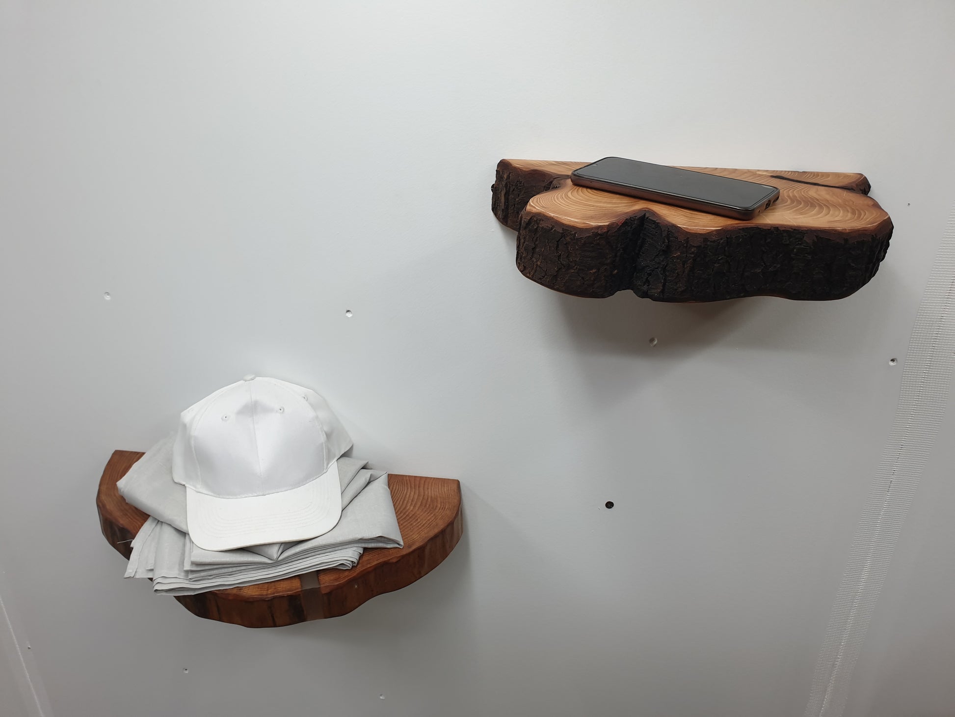 a pair of half log ring wooden shelves with a phone placed on one and a baseball cap and tablecloth on the other