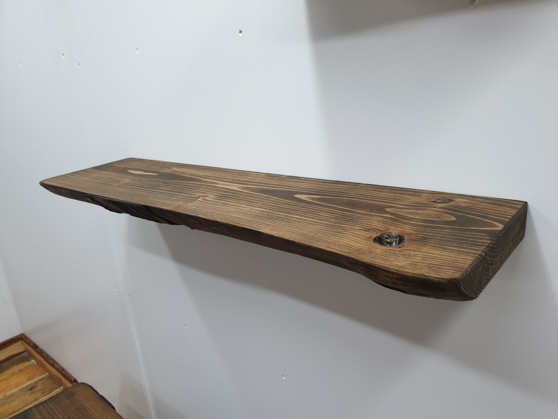 A closeup of a floating wall shelf with a dark oak stain