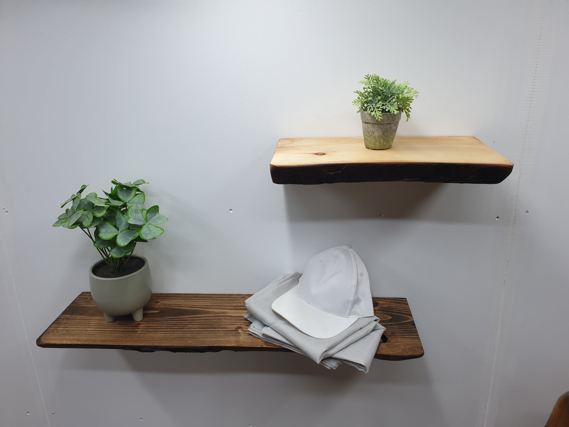 A pair of wooden floating shelves. The upper shelf is shorter and retains its natural colour while the lower shelf is longer and has been treated with a dark oak stain.