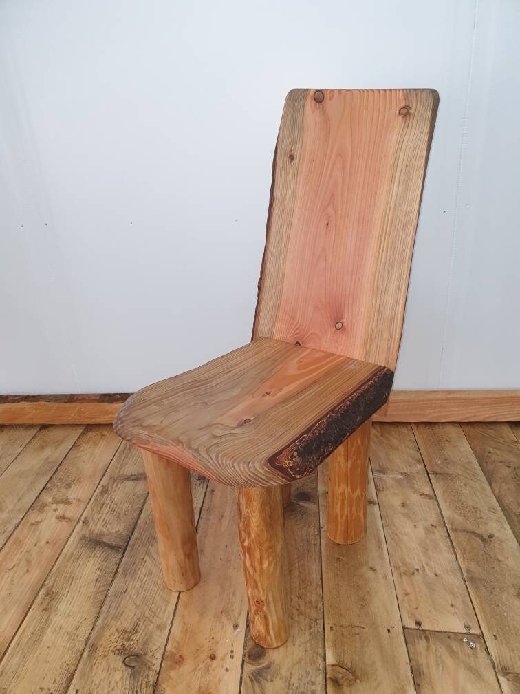 A short wooden chair with a reclined back on a wooden floor and a white studio background. The chair has noticeably red heartwood.