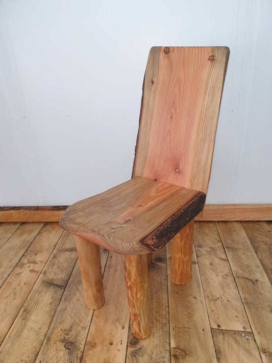 A short wooden chair with a reclined back on a wooden floor and a white studio background. The chair has noticeably red heartwood.