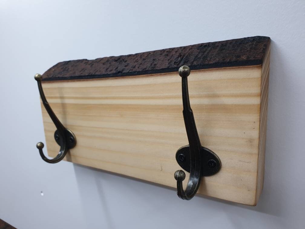 A close up of a 2 hook coat rack from the right aspect. It has sandy coloured wood grain and a thin dark brown bark layer along the top.