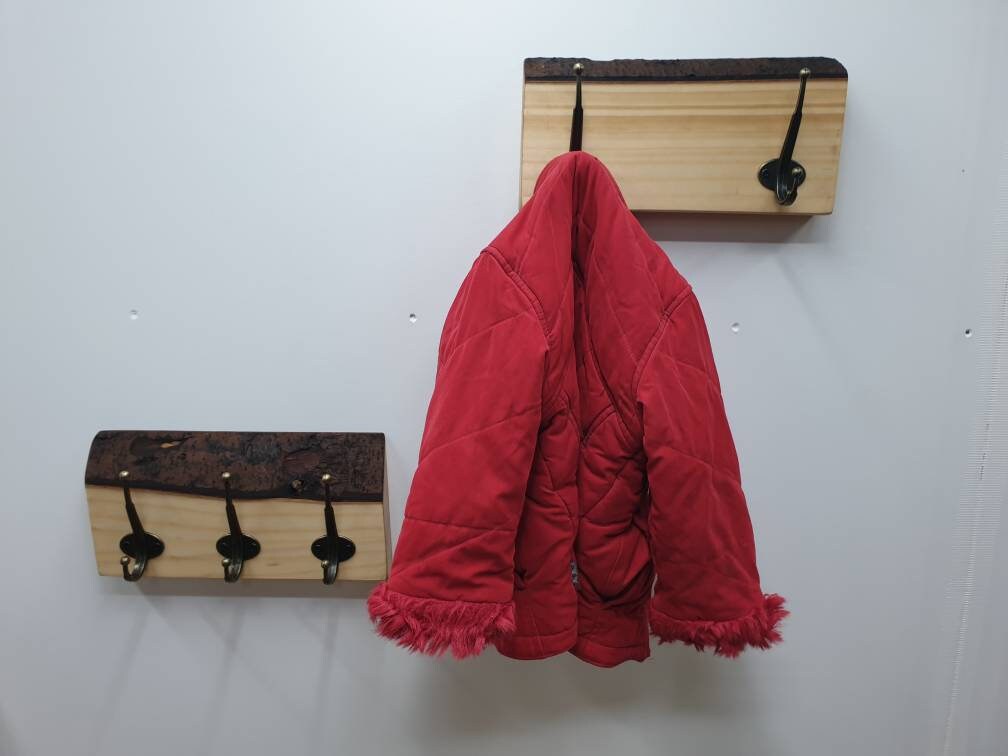 A photo of 2 coat racks mounted on a wall. 1 has 2 hooks with a red childs coat hung on one of them. The other is mounted slightly lower and to the side which has 3 hooks and nothing hanging from it.
