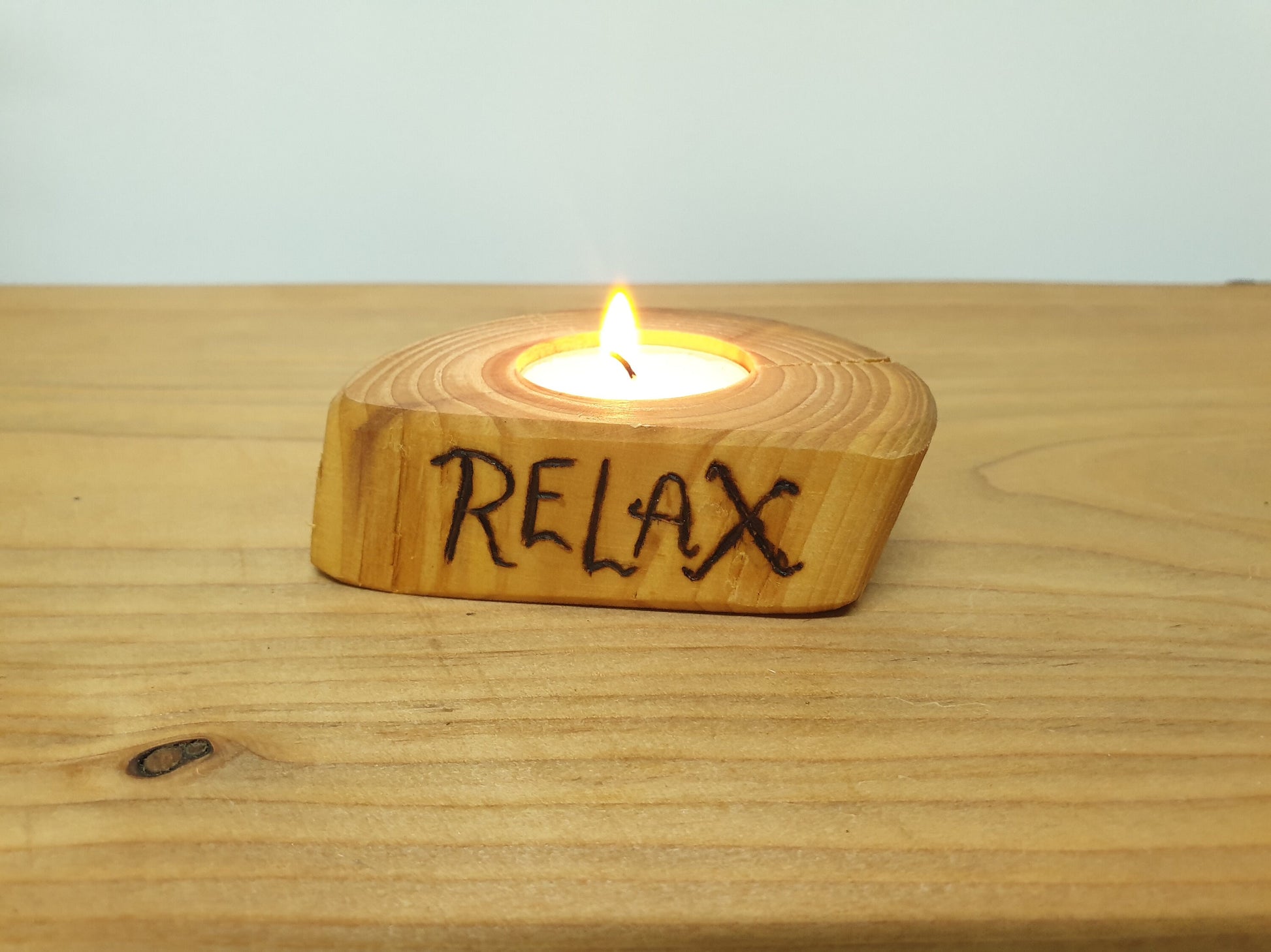 A lit tea light in a log tea light holder with the word "Relax" burned into the side